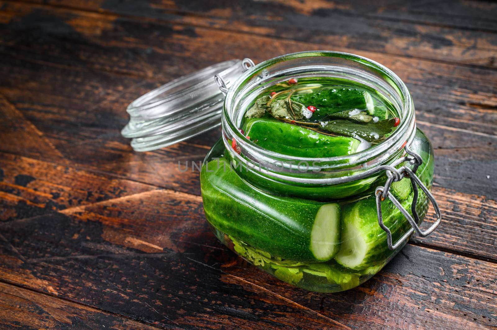 Green salted cucumbers in a glass jar. Canned vegetables. Dark Wooden background. Top view