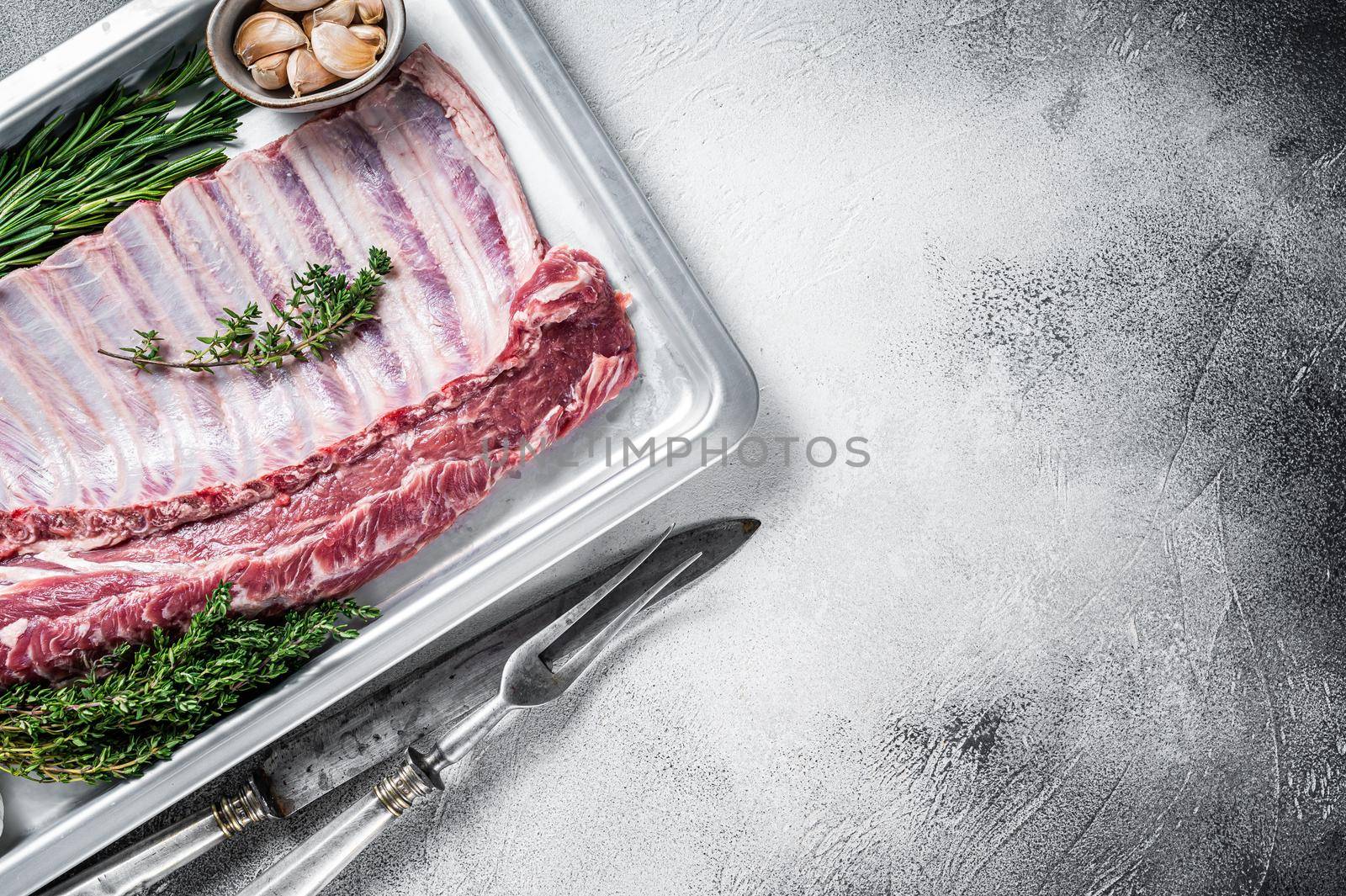 Uncooked raw rack of lamb ribs in baking dish with herbs. White background. Top view. Copy space by Composter