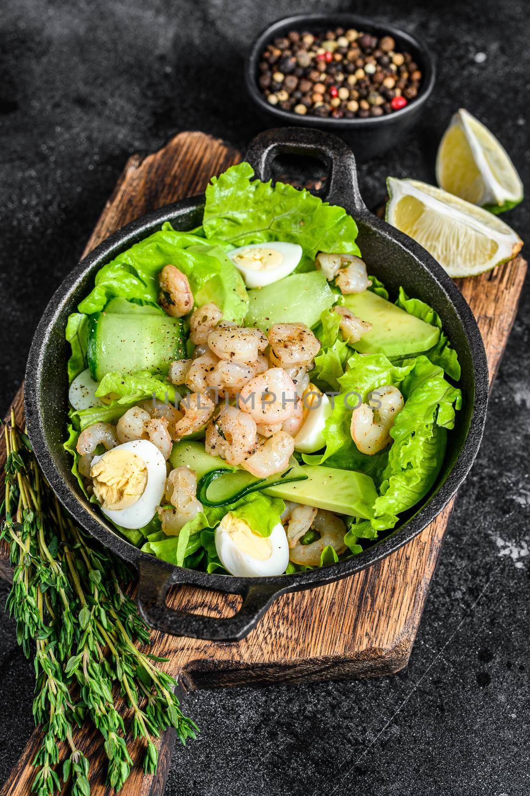 Seafood salad with grilled shrimps prawns, egg, avocado and cucumber in a pan. Dark wooden background. top view.