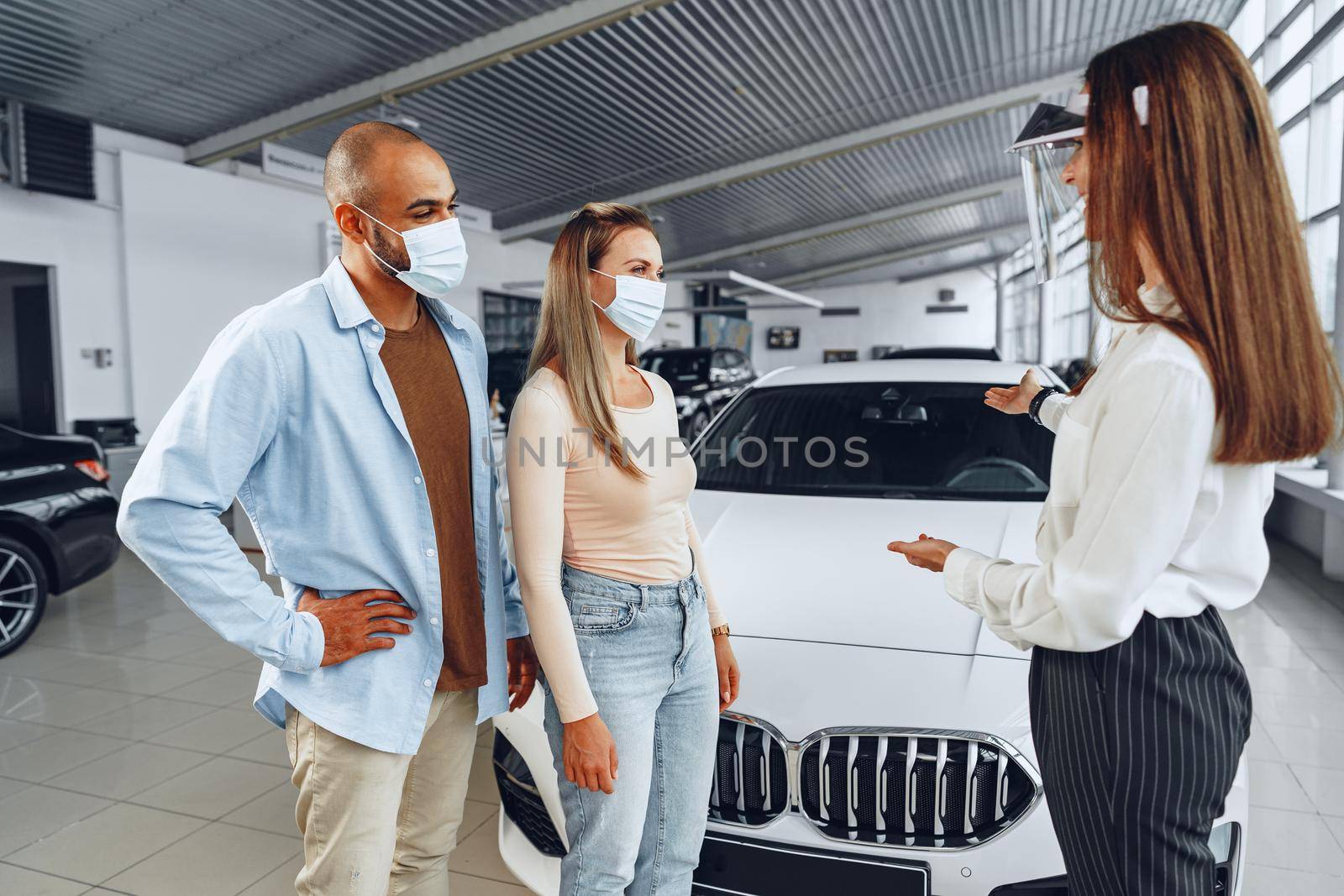 Woman car dealer consulting buyers wearing medical face shield by Fabrikasimf