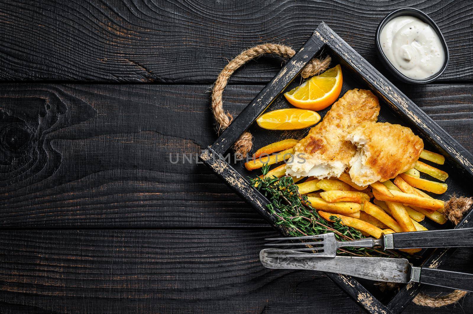 Battered Fish and chips dish with french fries and tartar sauce in a wooden tray. Black wooden background. Top view. Copy space by Composter