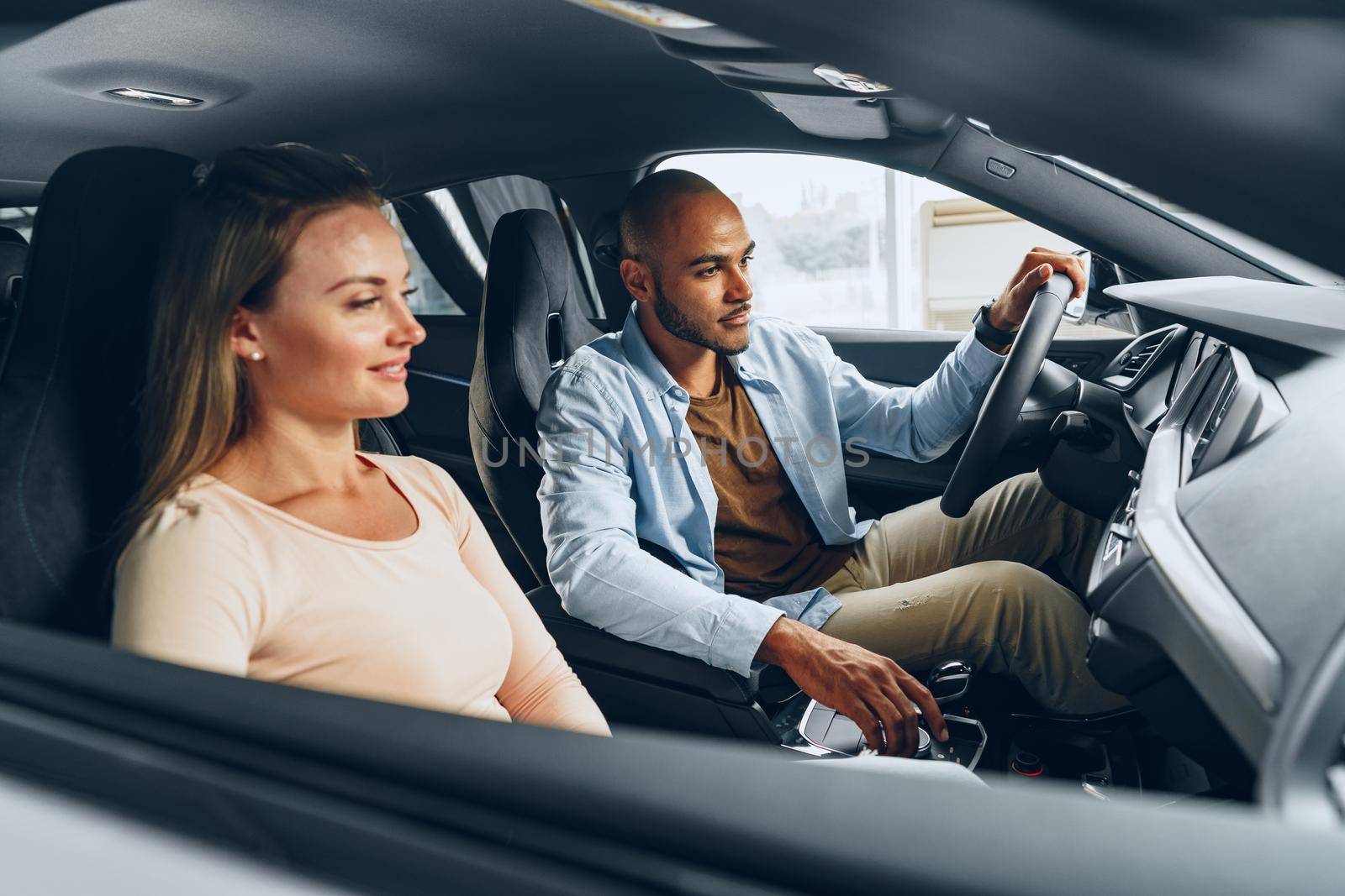 Joyful young couple looking around inside a new car they are going to buy in a car shop dealership