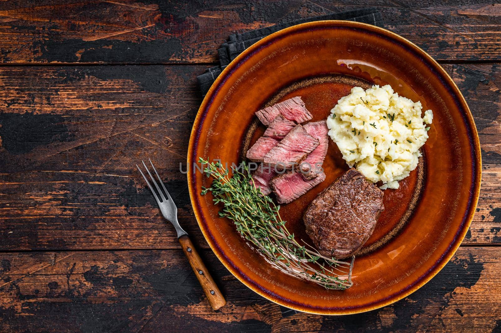 Sliced fillet mignon or tenderloin beef steak on a rustic plate with mashed potato. Dark wooden background. Top view. Copy space.