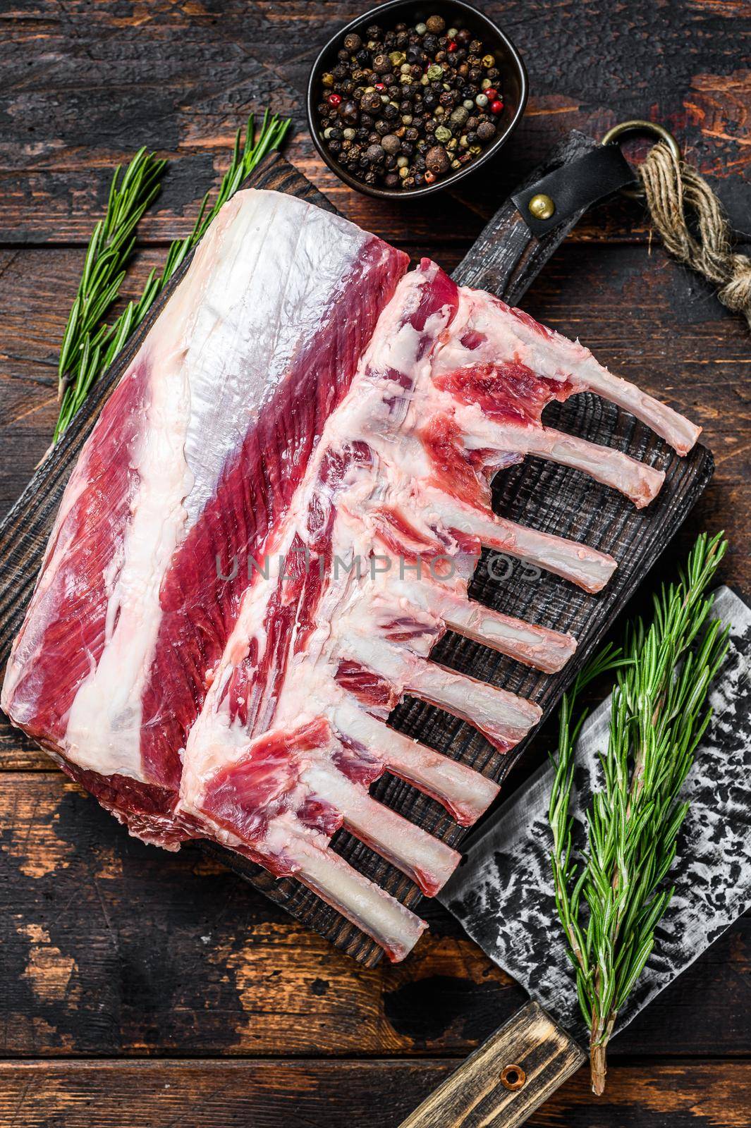 Rack of lamb raw meat with bone on a cutting board. Dark wooden background. Top view by Composter