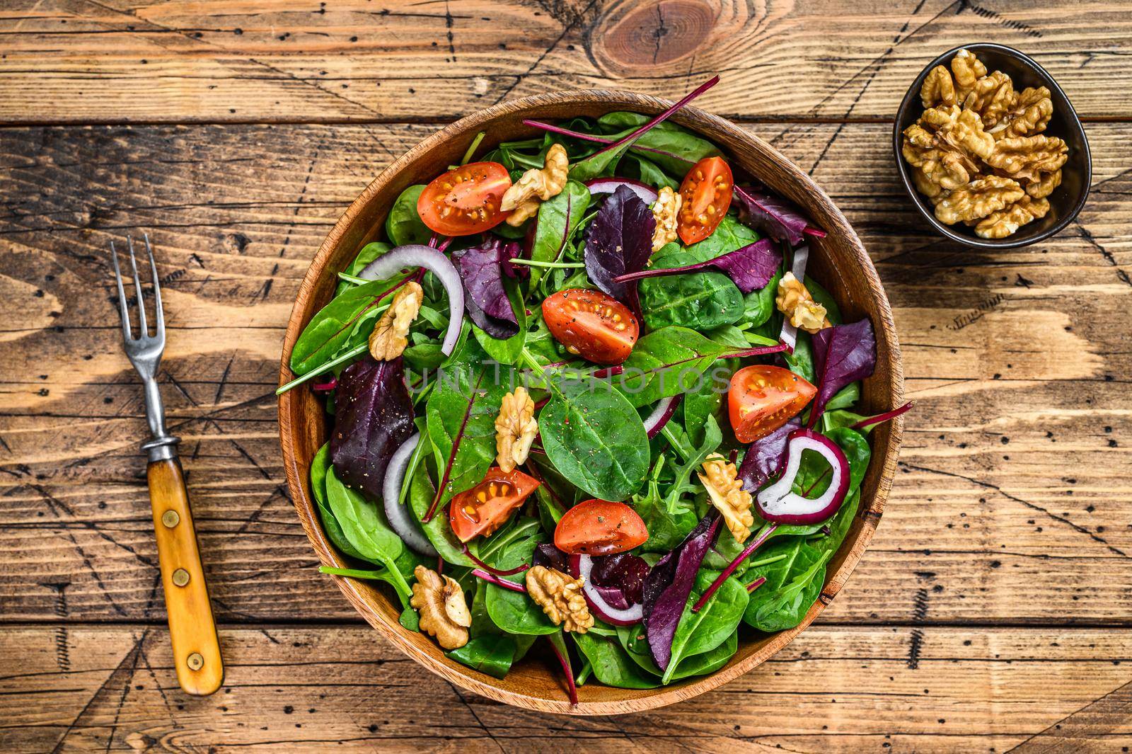 Fresh vegetable green salad with leaves mangold, swiss chard, spinach, arugula and nuts. wooden background. Top view.