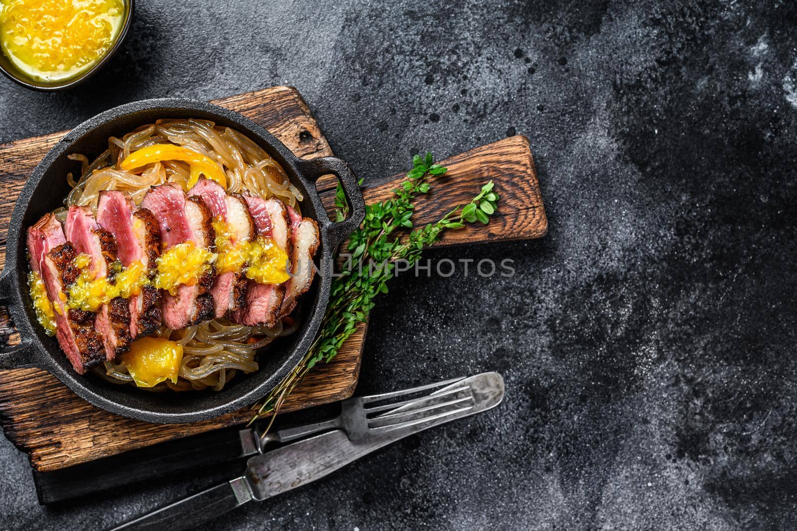 Grilled duck meat breast fillet steak with noodles and tangerines sauce. Black background. Top view. Copy space by Composter