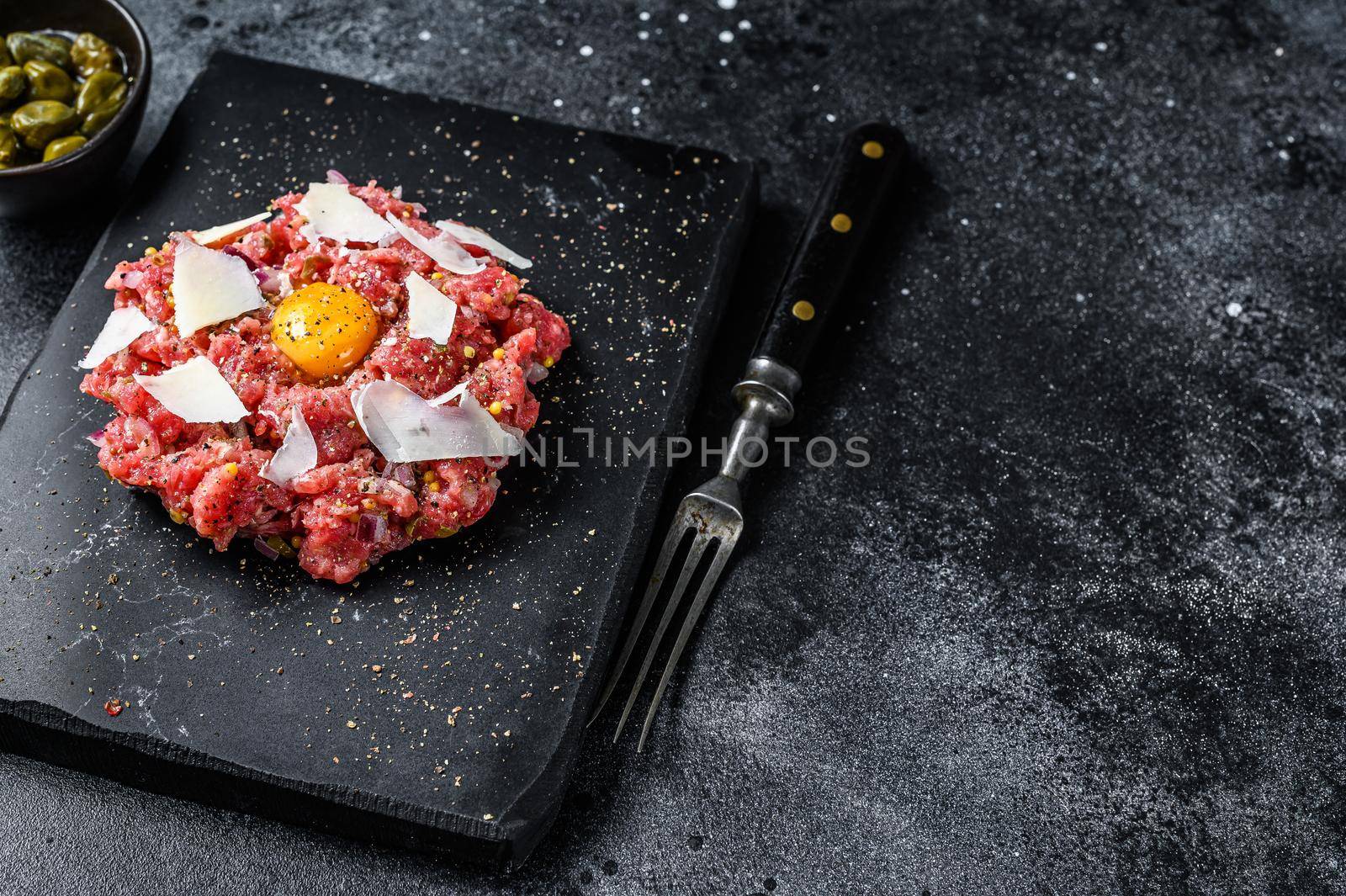 Tartar beef with a quail egg, capers and Parmesan cheese. Black background. Top view. Copy space by Composter