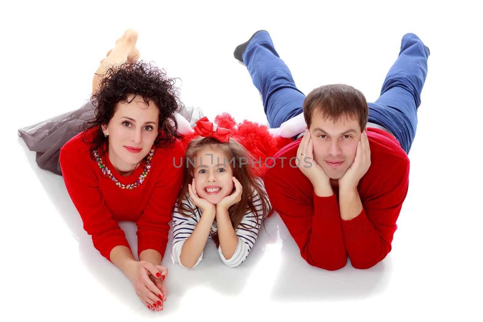 Happy young family dad mom and a little girl in bright red outfits . Family lying on the floor leaning on his hands.Isolated on white background.
