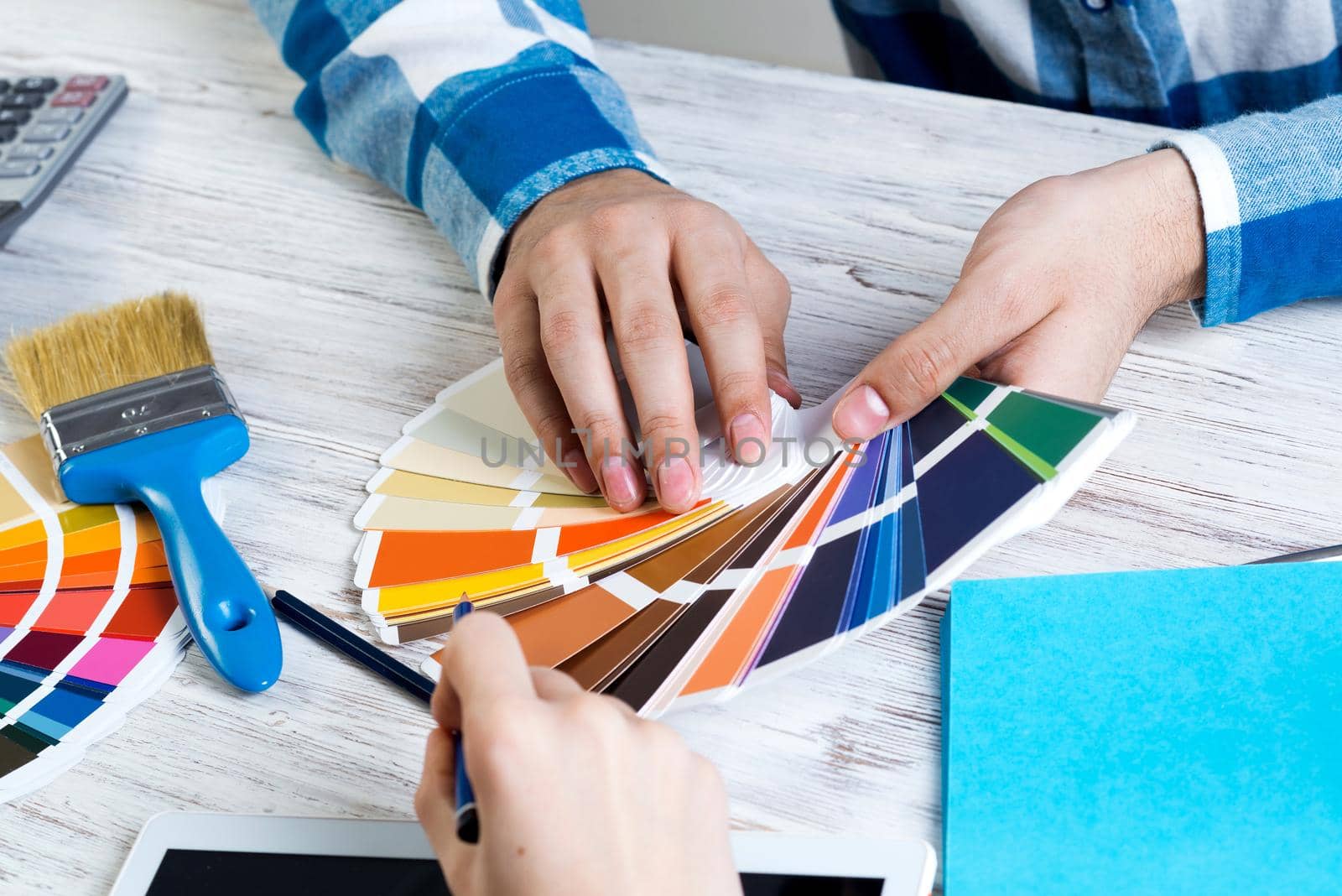Interior designer choosing colors from swatches at wooden desk. Office workplace in design studio. Selection of color palette for design. Professional house renovation and interior redesign.