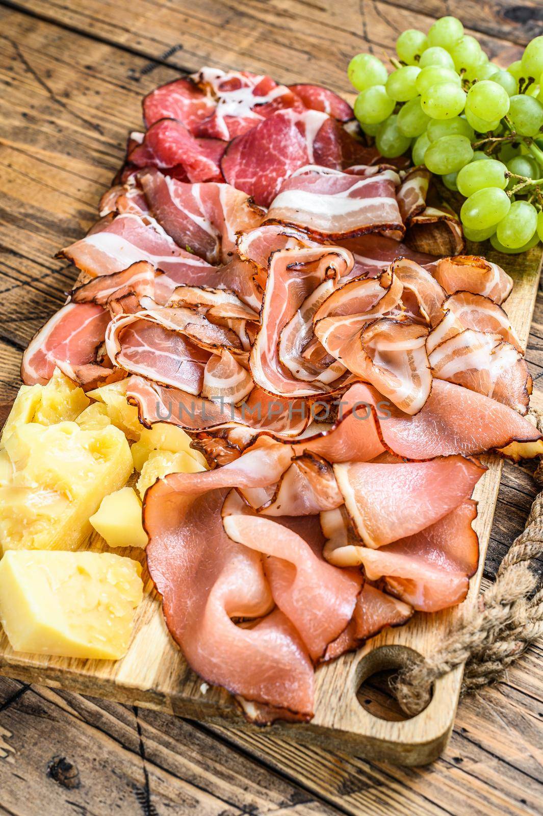 Meat antipasto board, pancetta, salami, sliced ham, sausage, prosciutto, bacon with grape and parmesan cheese. Wooden background. Top view.