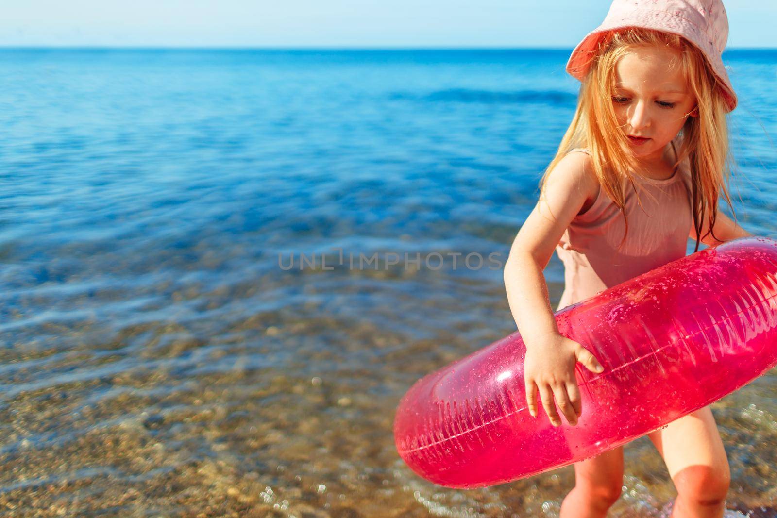 Happy little girl bathing in sea with pink circle and hat