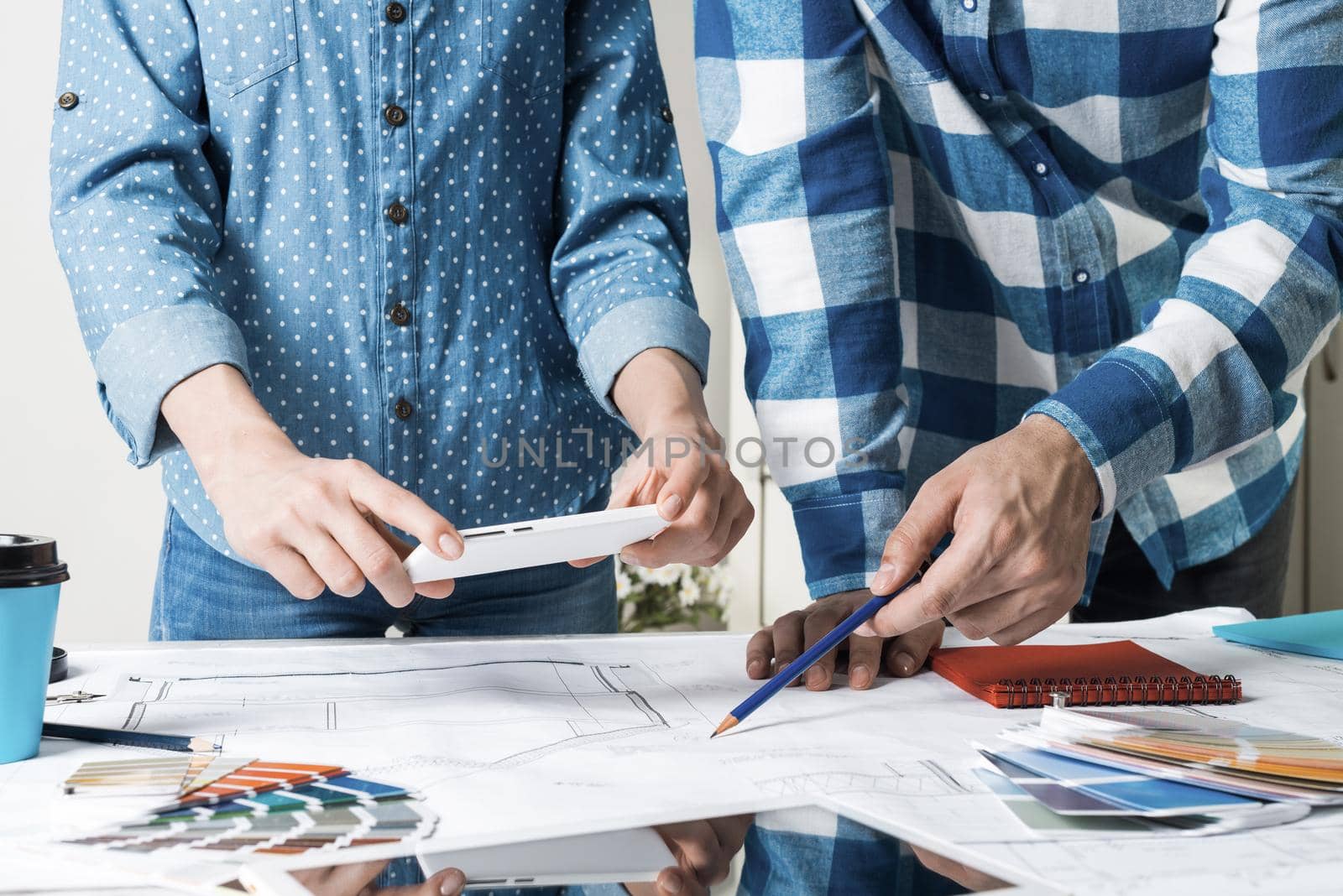 Woman taking photo of technical drawing with smartphone. Designers working with color swatches and construction blueprint at workplace. Interior design, architectural decoration and renovation.