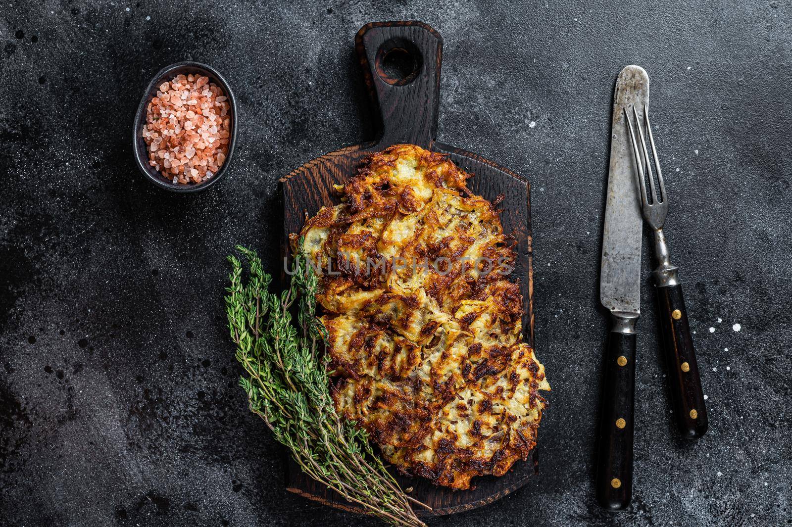 Potato pancakes with herbs and salt on wooden board. Black background. Top view.