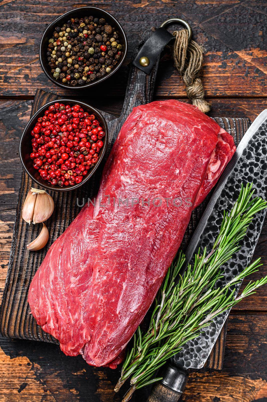 Whole Raw Tenderloin veal meat for steaks fillet mignon on a wooden cutting board with butcher knife. Dark wooden background. Top view.