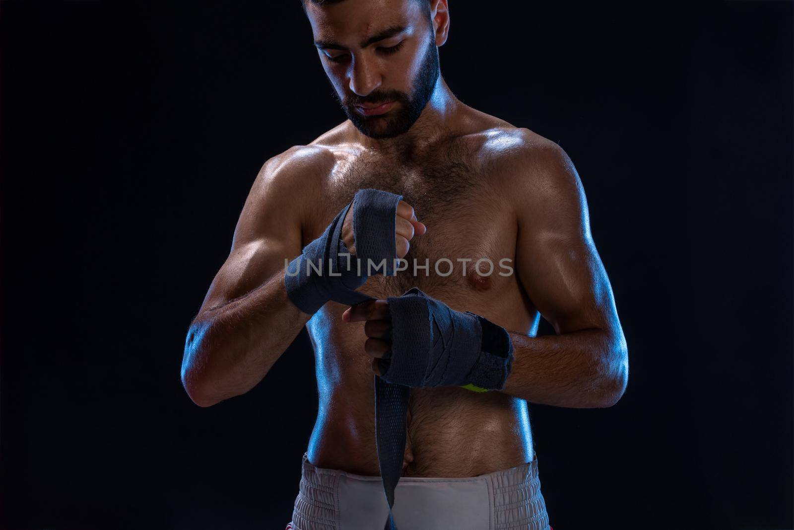 Sports boxer man pulls on the hand wrist wraps. Oriental male model isolated on black background. by nazarovsergey