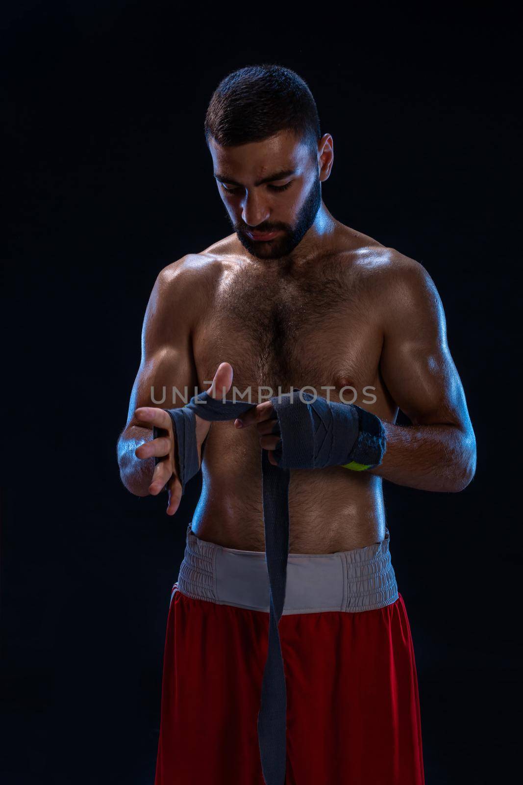Sports boxer man pulls on the hand wrist wraps. Oriental male model isolated on black background. by nazarovsergey