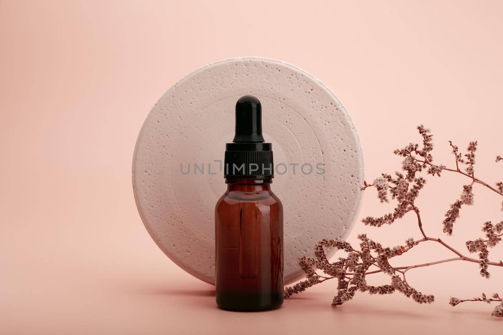Skin serum or oil in dark brown glass bottle with round gypsum circle and dry flower against beige background by Senorina_Irina