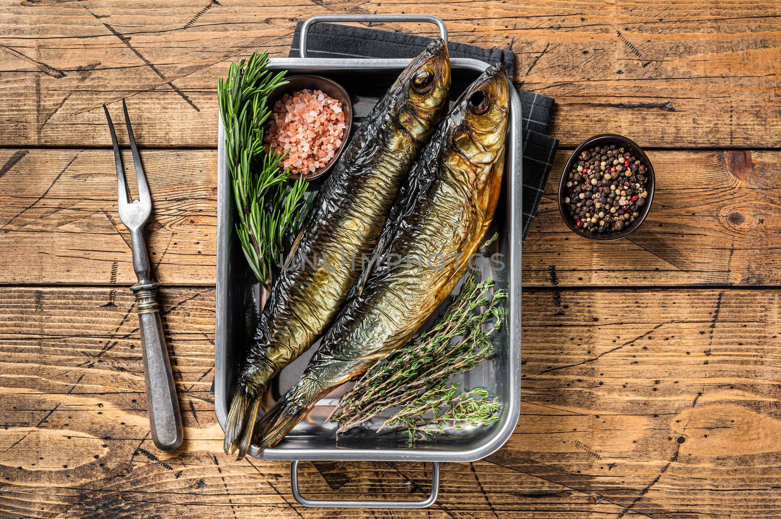 Smoked marinated herring fish in kitchen tray with herbs. Wooden background. Top view.