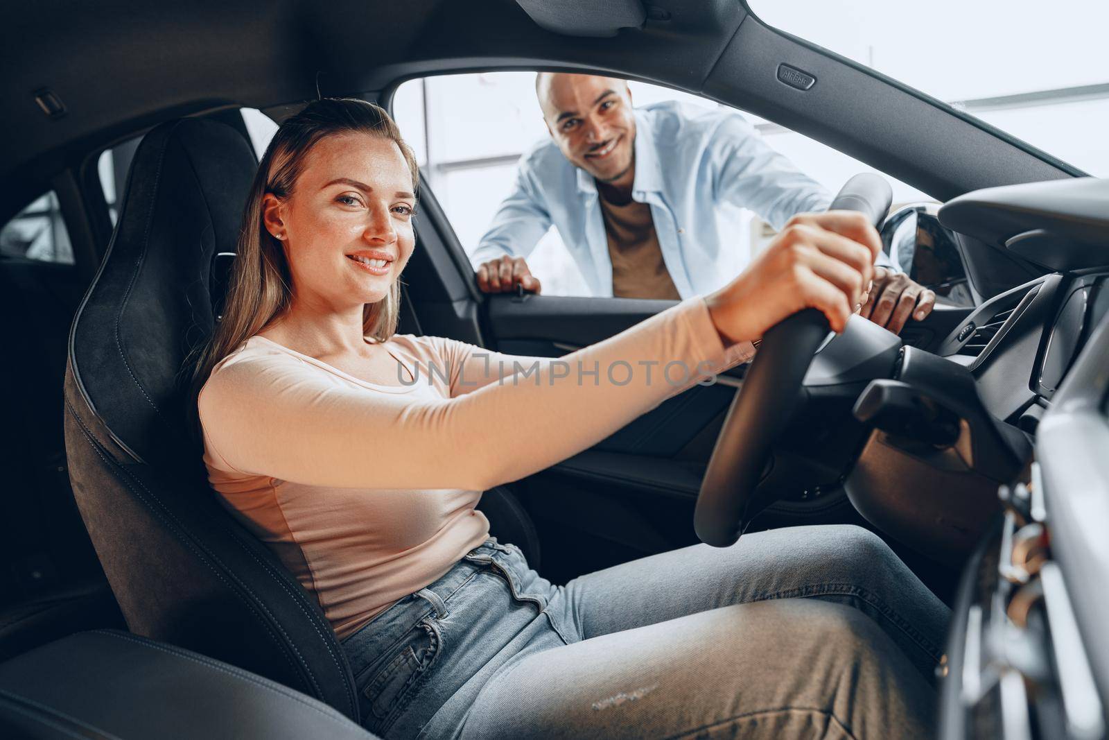 Joyful young couple looking around inside a new car they are going to buy in a car shop dealership