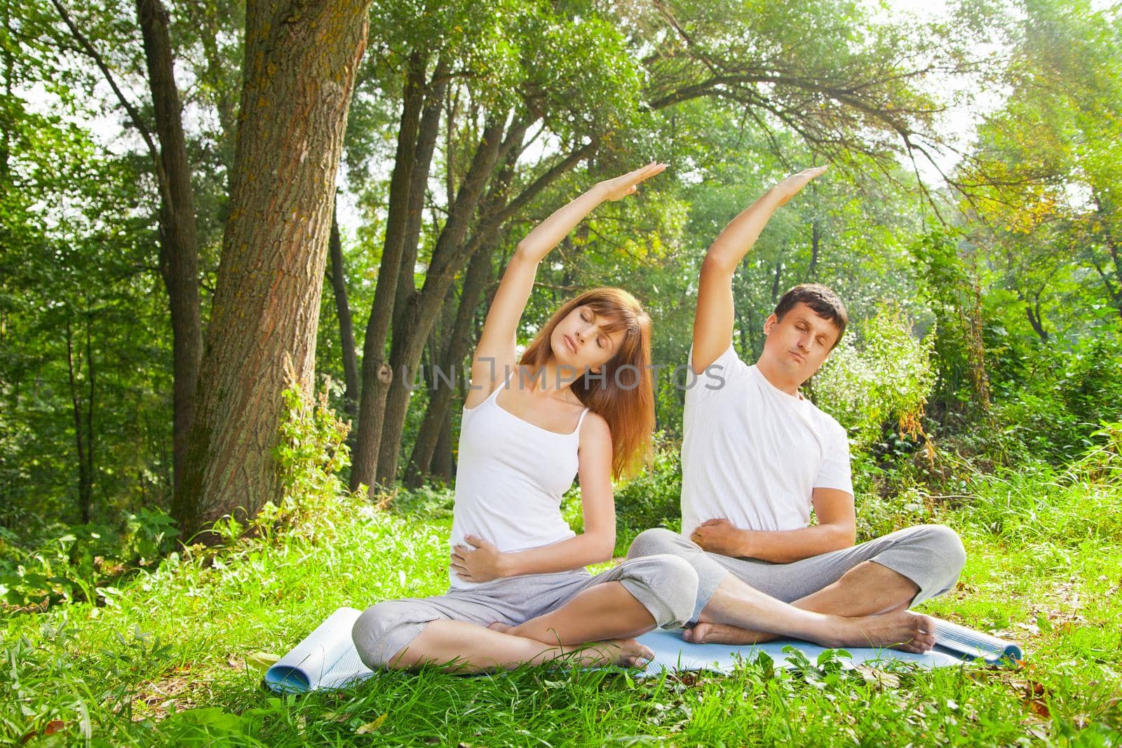 Young man and woman doing yoga in garden by Julenochek