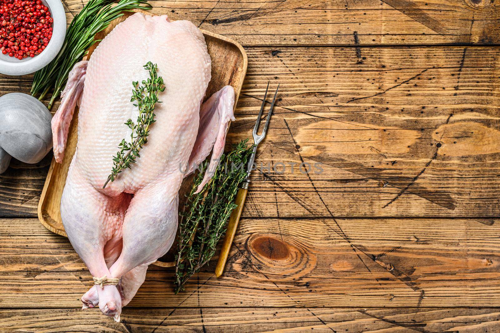 Raw whole farm duck with herbs. wooden background. Top view. Space for text.