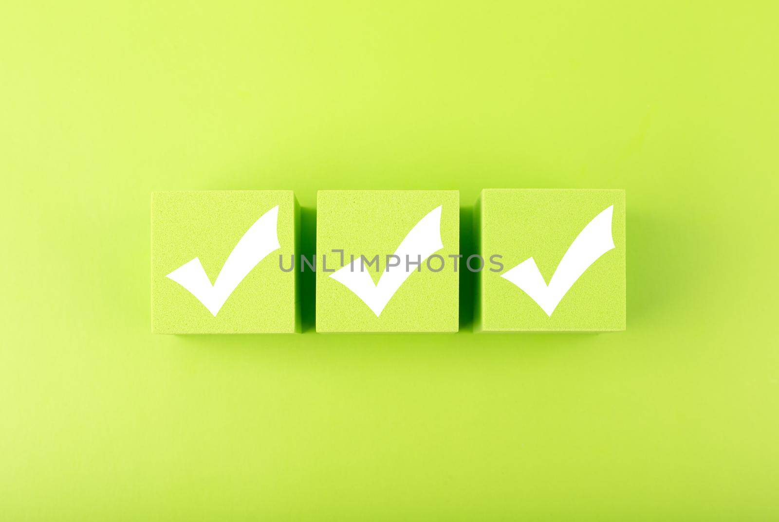 Three white checkmarks on green toy cubes on bright background. Concept of questionary, checklist, to do list, planning, business or verification.