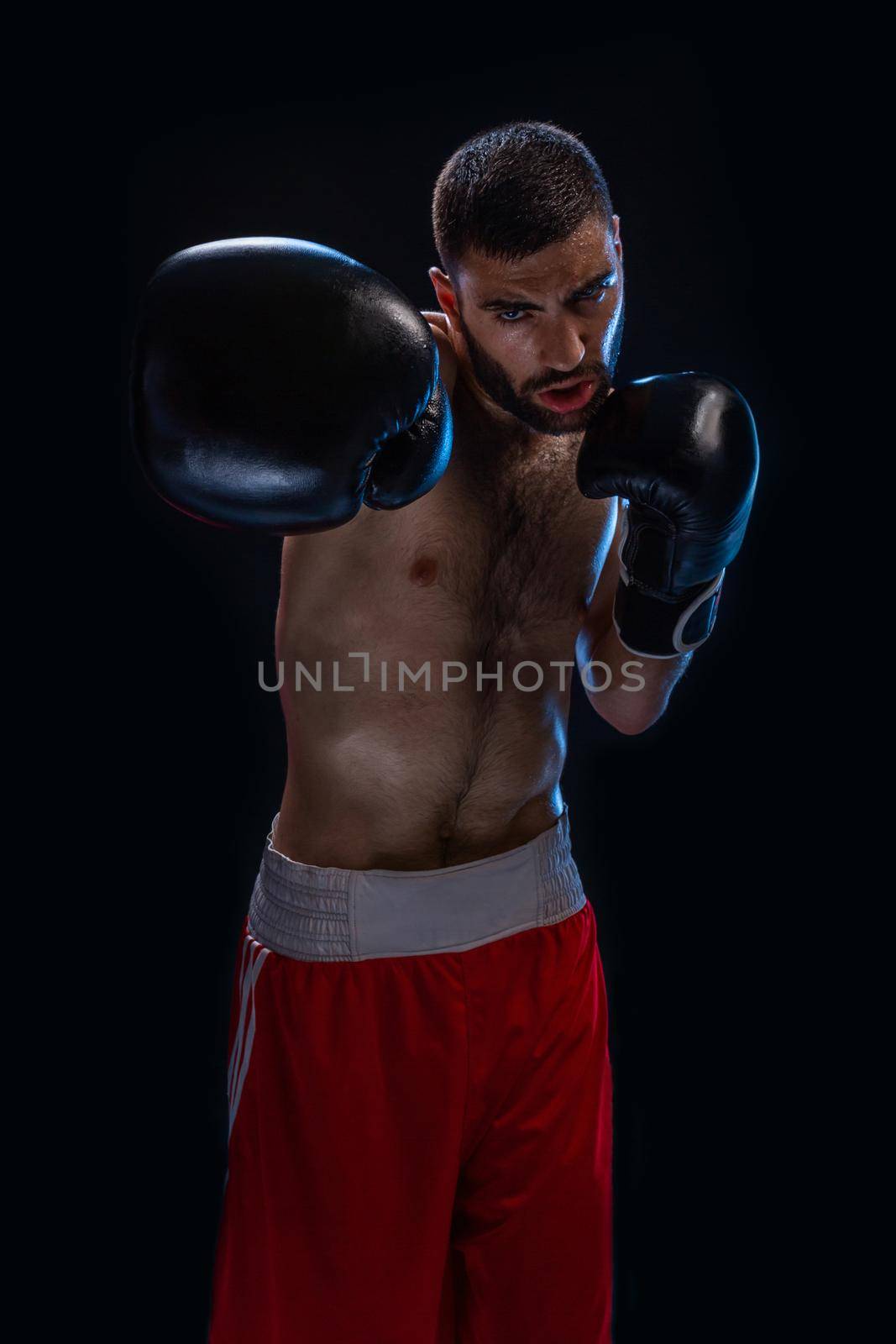 The boxer is ready to deal a powerful blow. Photo of muscular man on black background. Strength and motivation.
