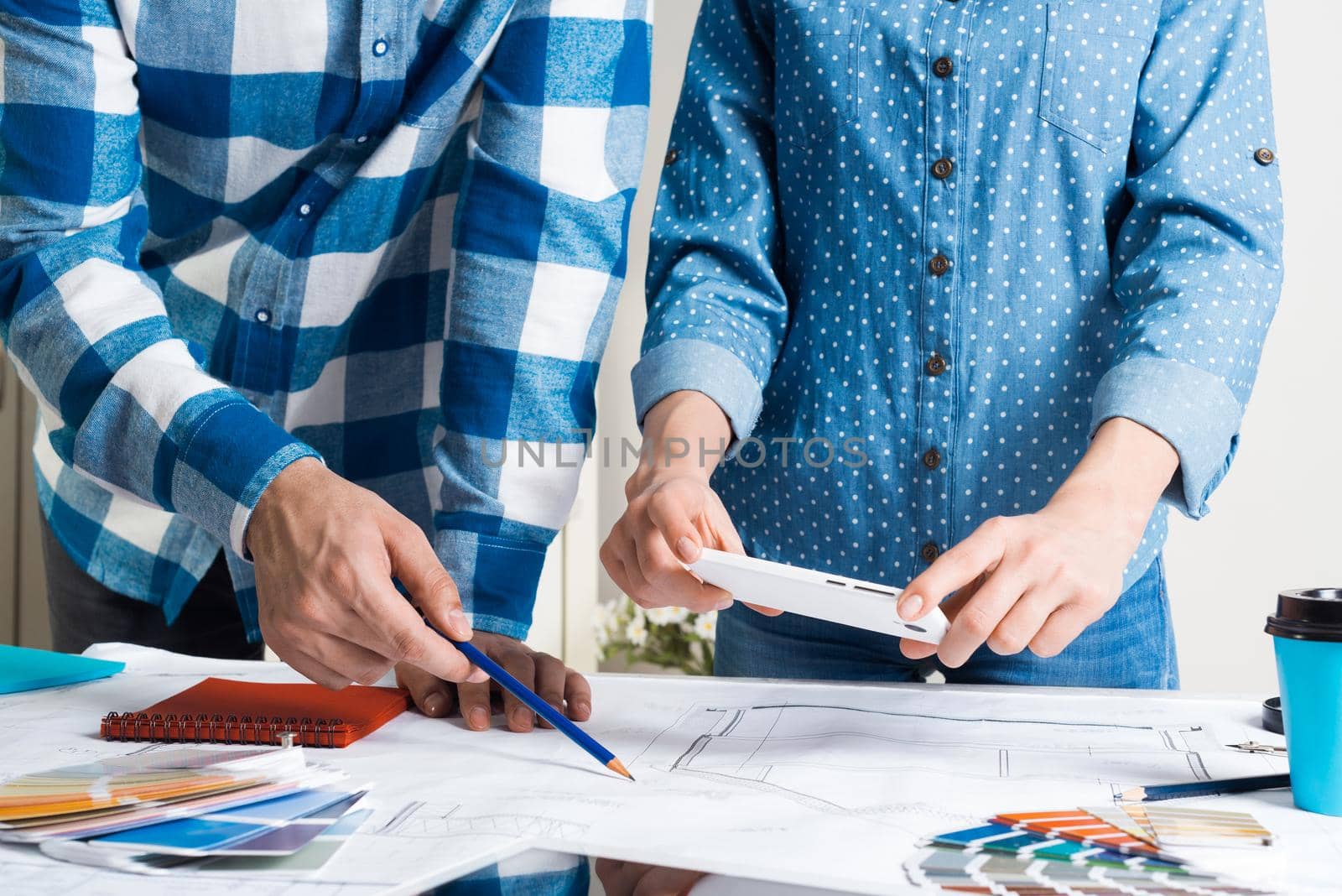 Woman taking photo of technical drawing with smartphone. Designers working with color swatches and construction blueprint at workplace. Interior design, architectural decoration and renovation.