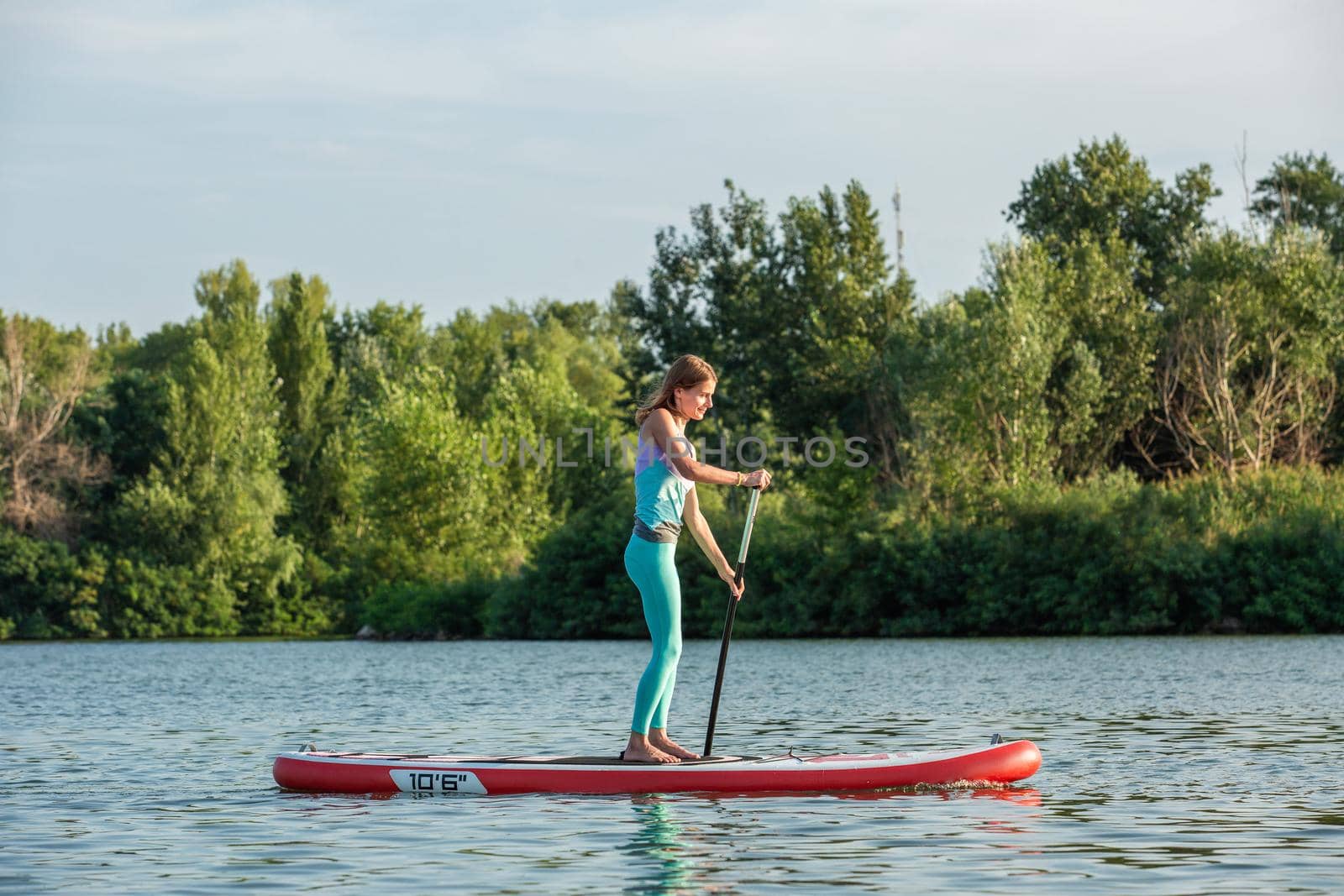 Confident woman standing with a paddle on the surfboard, SUP. Sport. Hobby. Yoga.