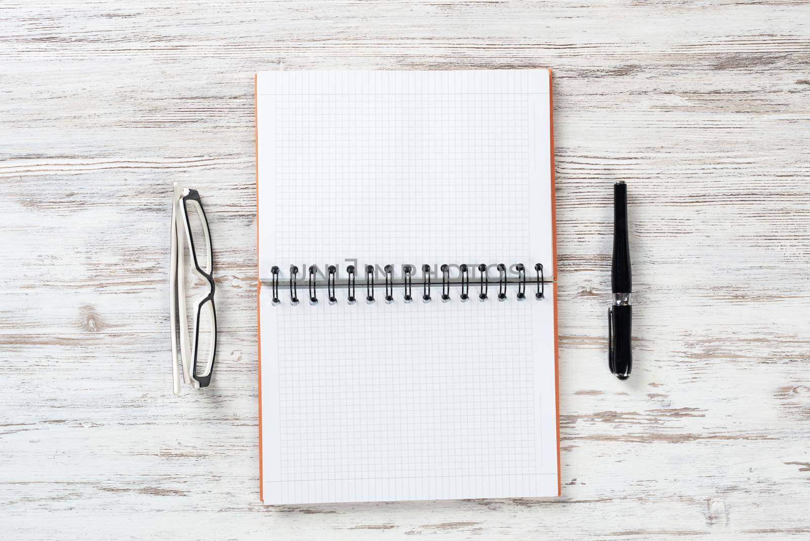 Still life of modern office workspace with supplies. Flat lay grunge wooden desk with open spiral notebook, glasses and pen. Time management and day planning concept. Blank notebook page for message.