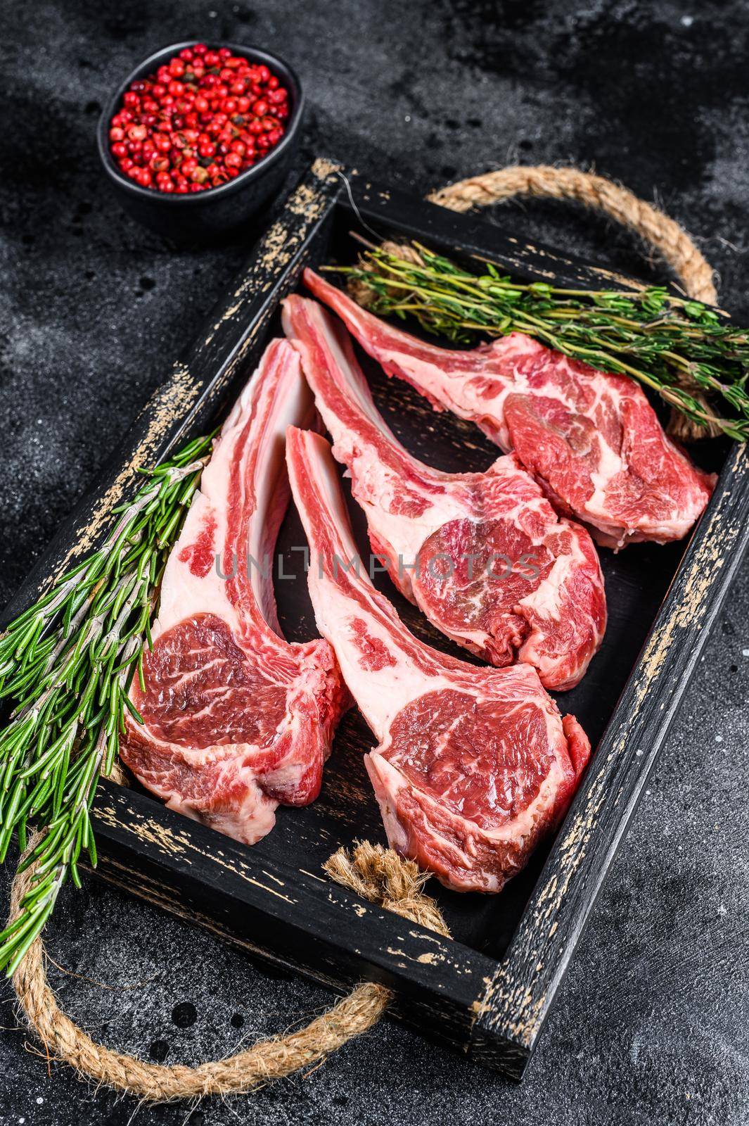 Raw lamb meat chops steaks in a wooden tray. Black background. Top view by Composter