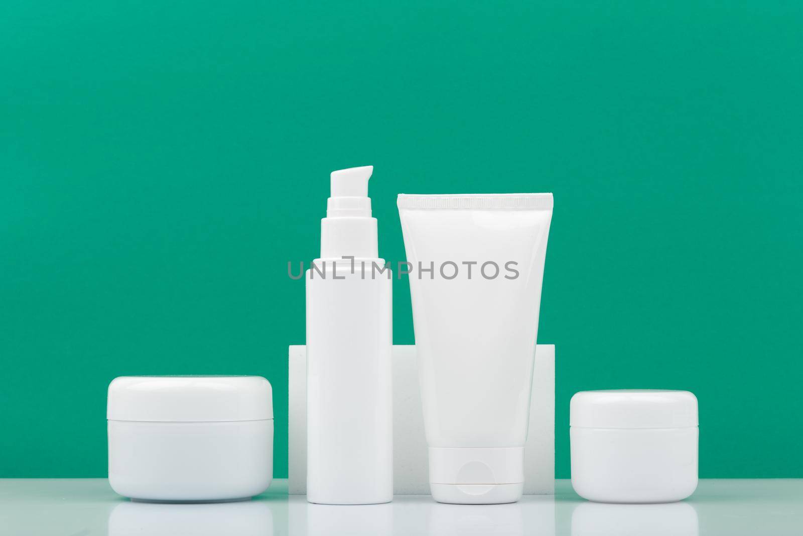 Set of white unbranded cosmetic bottles for daily skincare against dark green background. Concept of hygiene, man's skin care or anti acne treatment