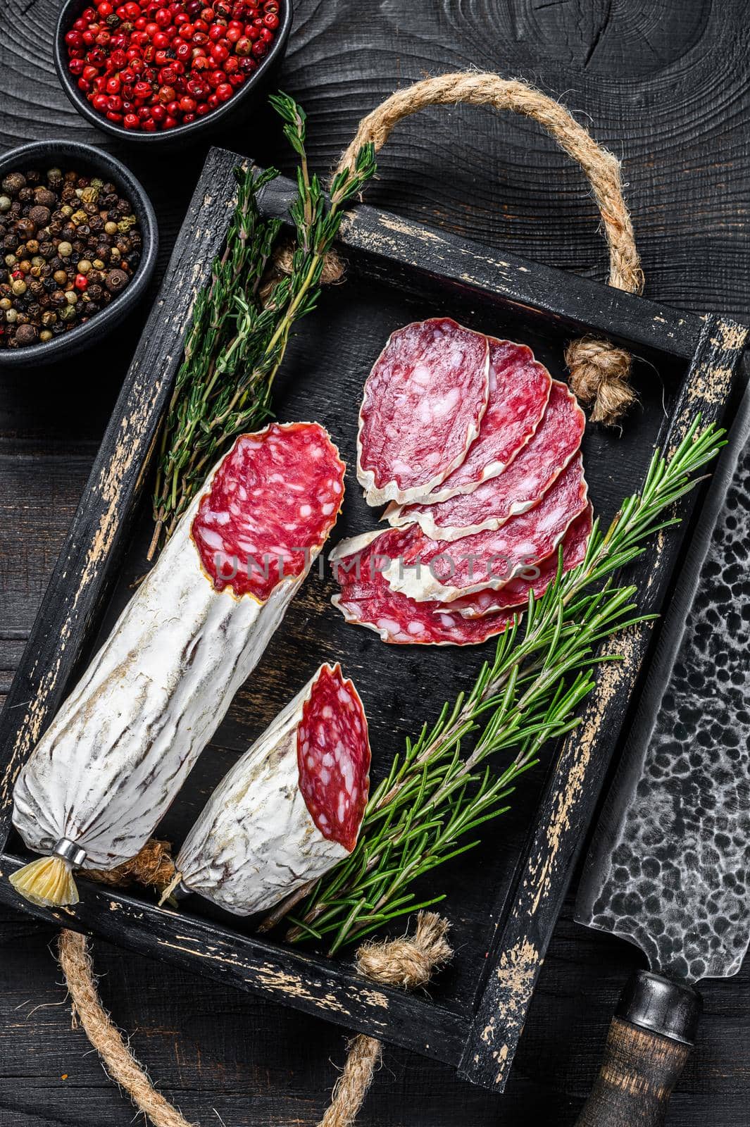 Slices of dry cured salchichon salami in a wooden tray. Black wooden background. Top view.