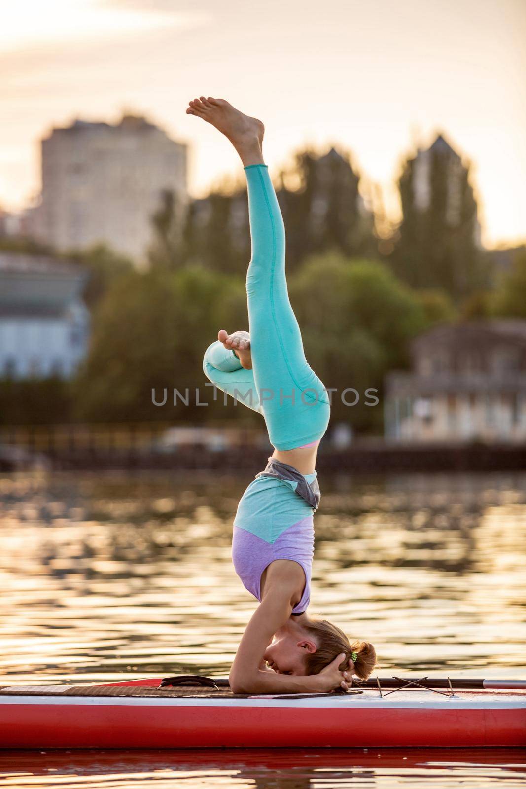 Sporty woman in yoga position on paddleboard, doing yoga on sup board, exercise for flexibility and stretching of muscles. Woman practicing yoga on the paddle board in the morning
