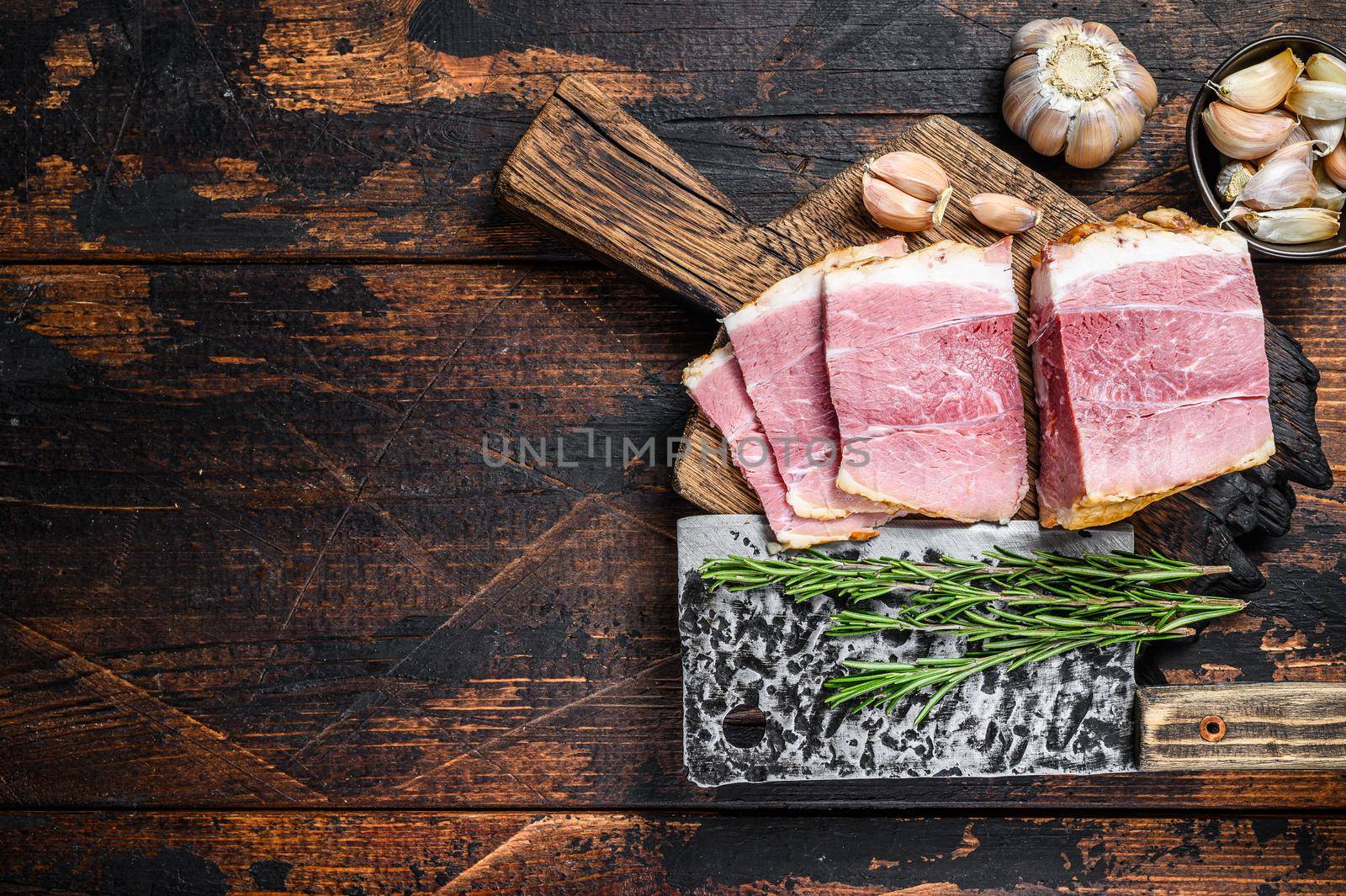 Smoked pork gammon meat slices on a wooden rustic cutting board. Dark wooden background. Top view. Copy space by Composter