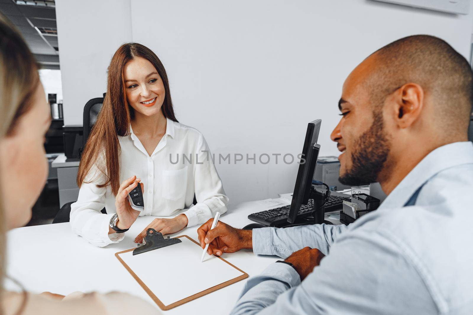 Young woman car seller showing contract to couple of car buyers in her office