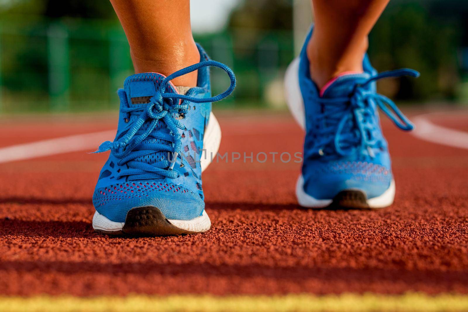 Close-up of woman's legs in blue sneakers on start before jogging. Red treadmill at the stadium