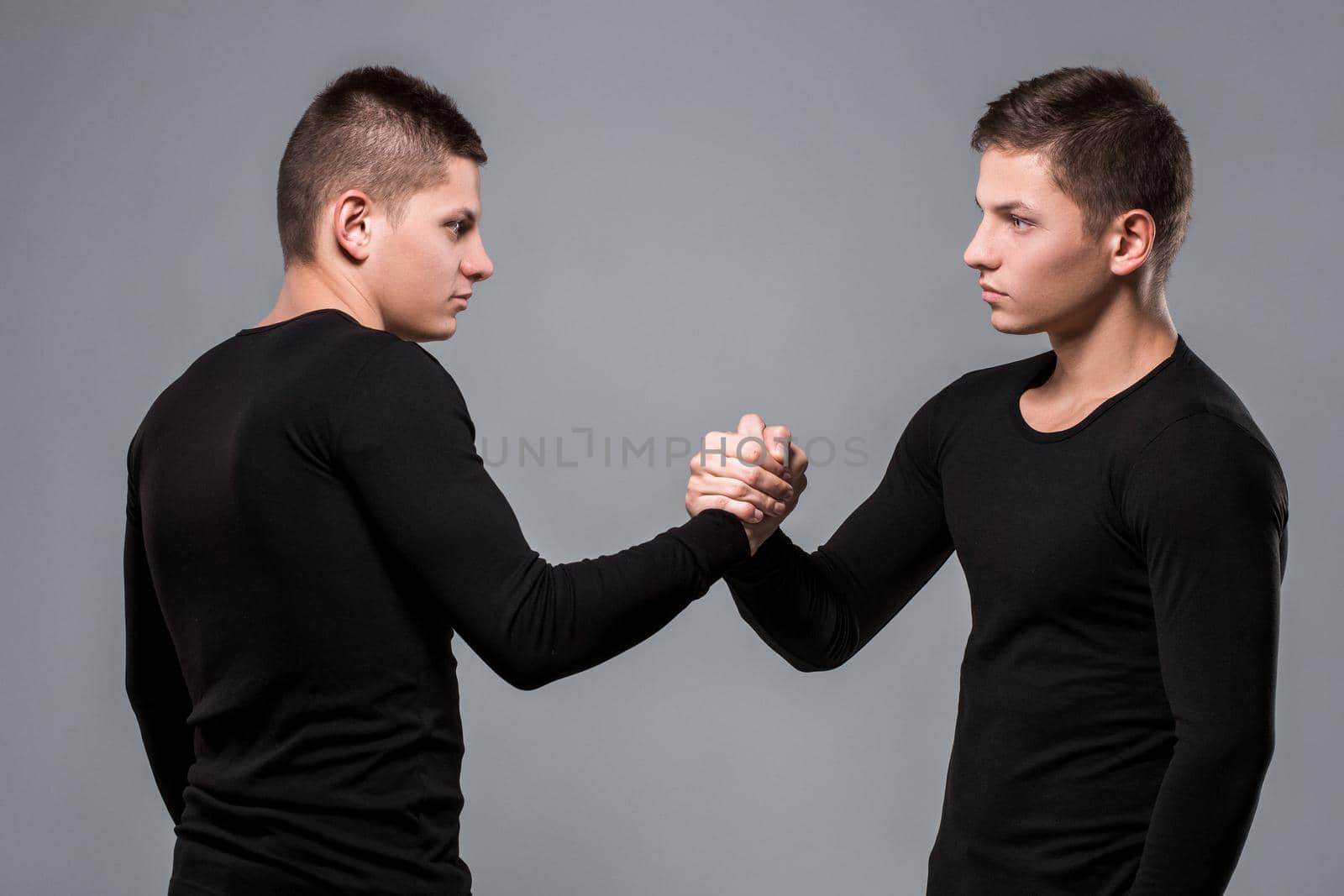Portrait of young twin brothers standing face to face on gray background. Copy space. Casual twin brothers.