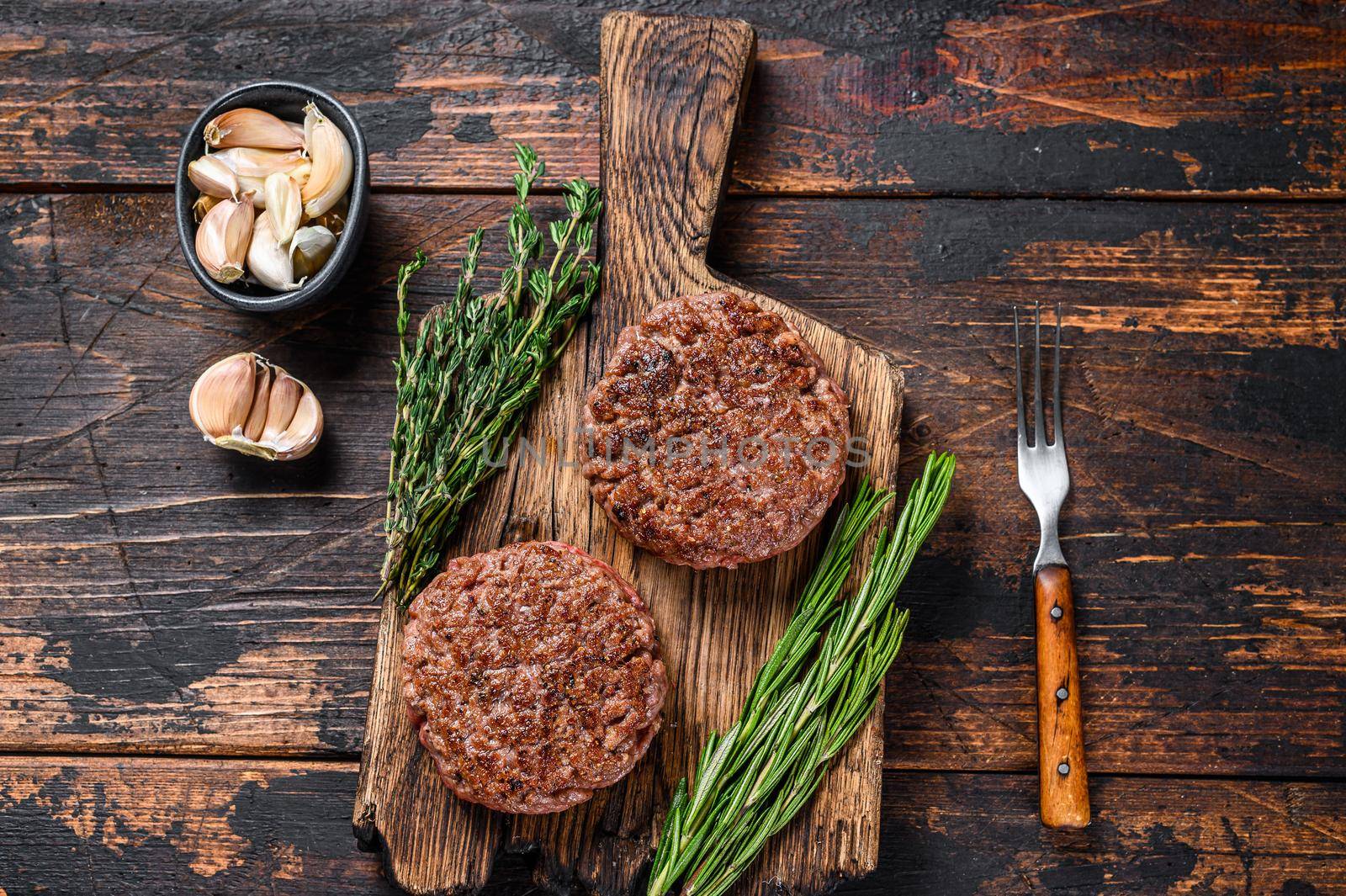 Barbecue steak patties for burger from ground beef meat on a wooden cutting board. Dark wooden background. Top view.