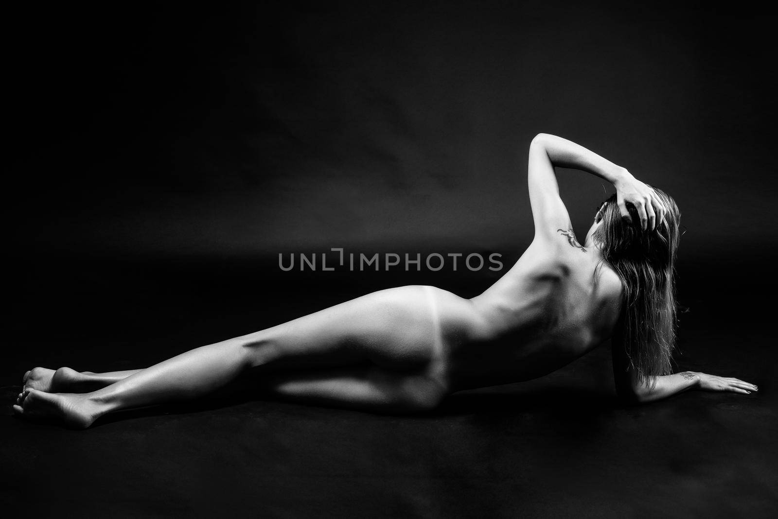 Young naked woman posing on black background. Perfect skin. Black and white photograph