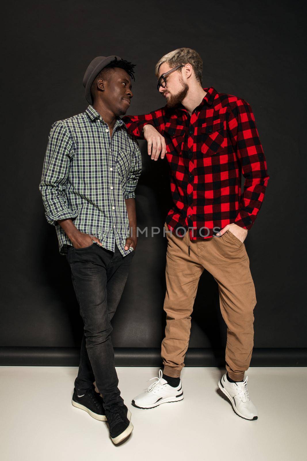 Studio lifestyle portrait of two best friends hipster boys going crazy and having great time together. On black background. Full-length photo