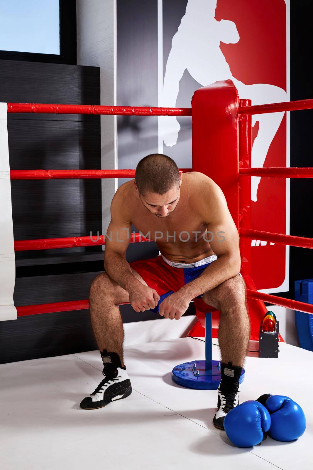 Tired male boxer sitting in the corner of the ring after a hard workout
