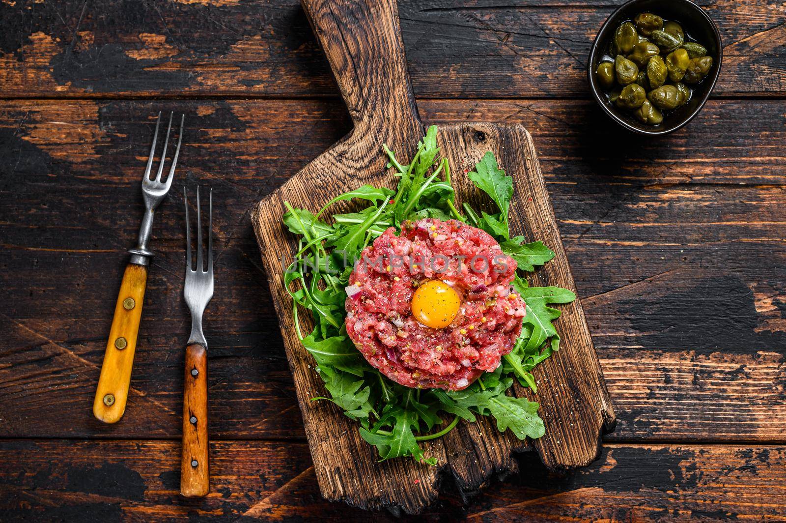 Tartar beef with a quail egg and arugula served on a cutting board. Dark wooden background. Top view by Composter