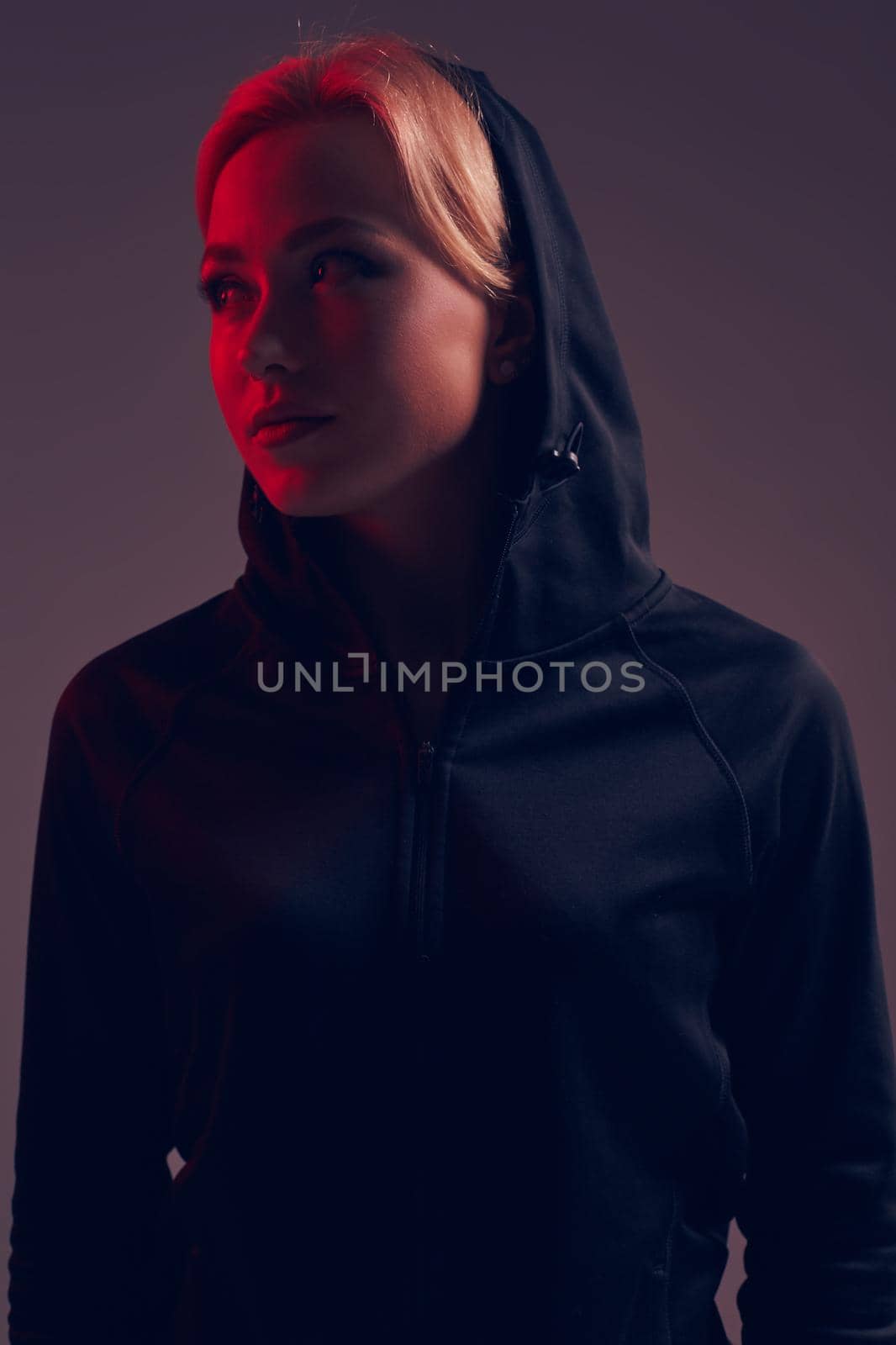 Young pretty woman wearing a black hood and shorts on dark background. olor filters. Studio shot.