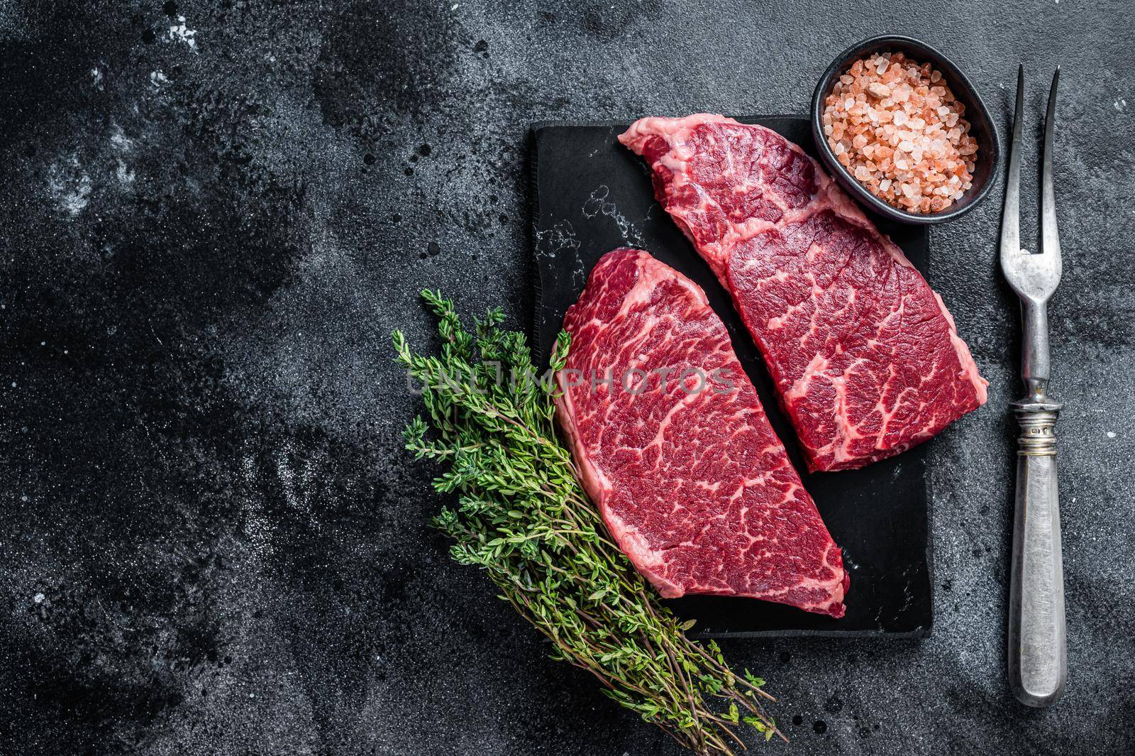 Fresh Raw Denver steak Marble beef meat with herbs. Black background. Top view. Copy space by Composter