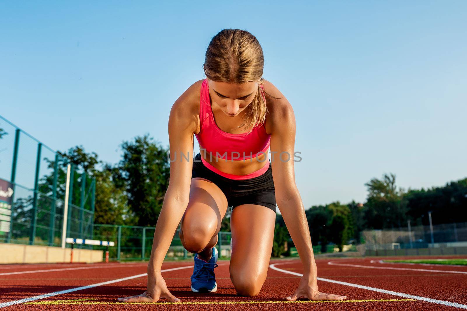 Young woman athlete at starting position ready to start a race. Female sprinter ready for sports exercise on racetrack.