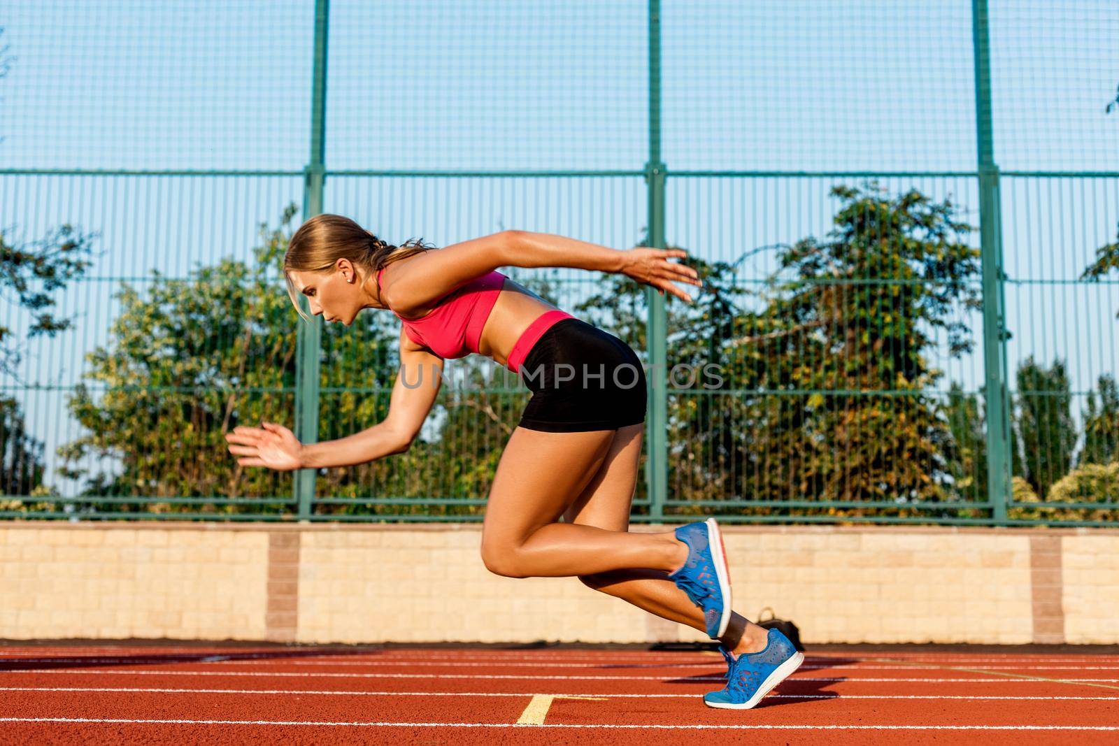 Portrait of beautiful woman ready to start running. Female athlete sprinter doing a fast sprint for competition on red lane at an outdoor field stadium.