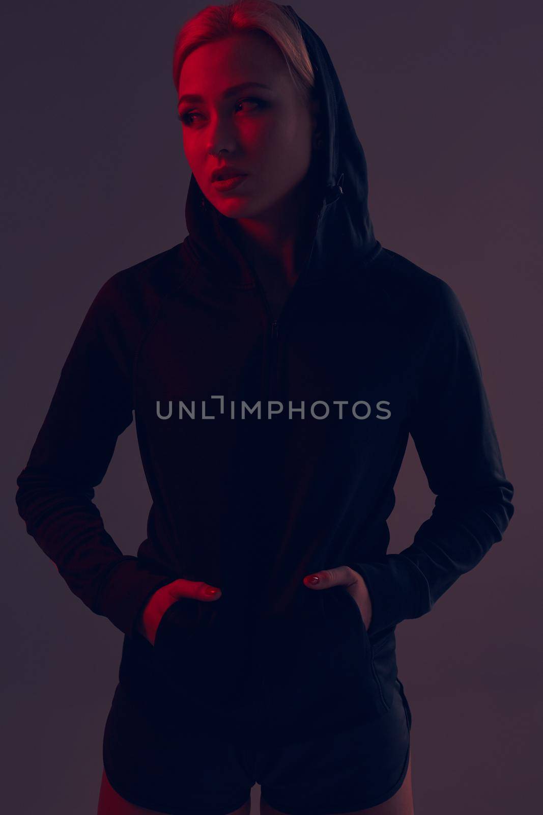 Beautiful seductive sporty girl with the slim sexy figure in the black hoodie, sport underwear and little black shorts is posing in the studio. olor filters.