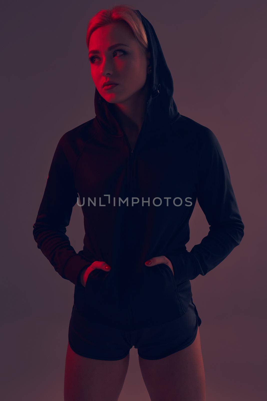 Beautiful seductive sporty girl with the slim sexy figure in the black hoodie, sport underwear and little black shorts is posing in the studio. color filters.