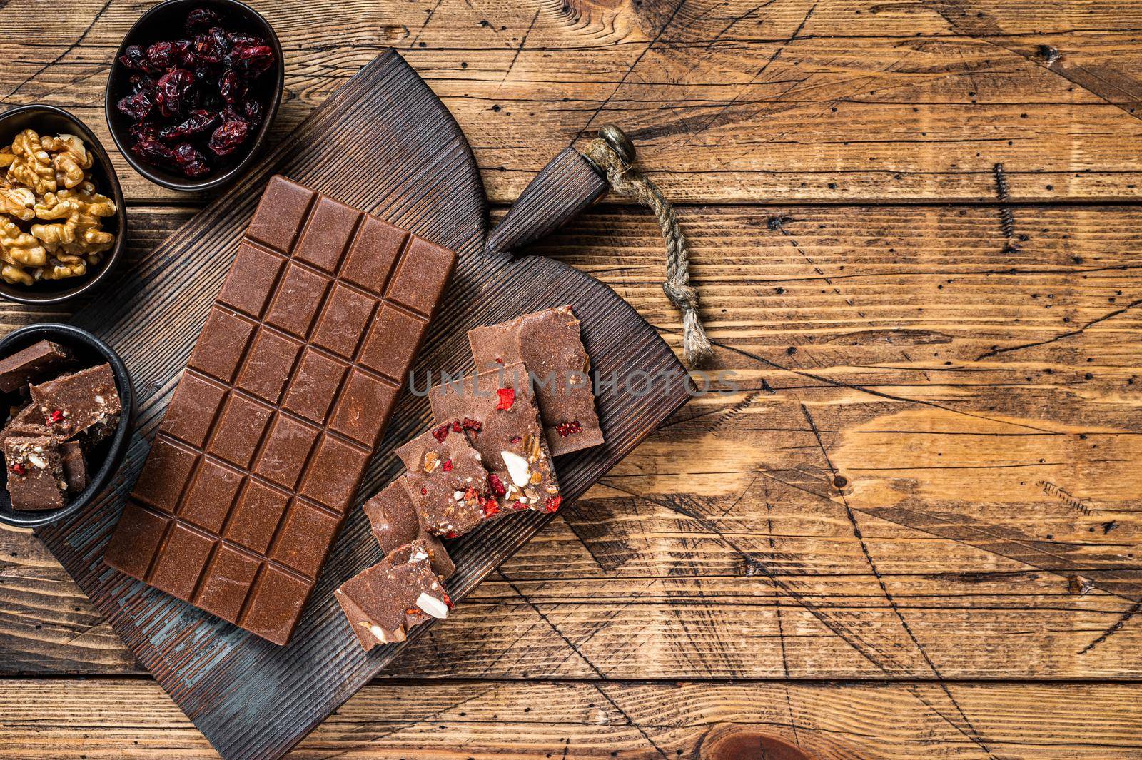Dark chocolate bar with hazelnuts, peanuts, cranberries and freeze dried raspberries on a wooden board. wooden background. Top view. Copy space by Composter
